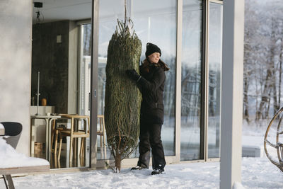 Woman carrying christmas tree in front of house