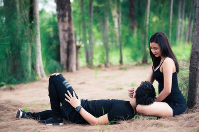 Young woman sitting on land against trees in forest