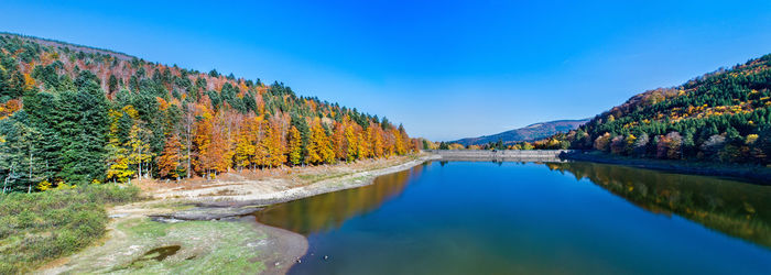 Panoramic view of lake amidst autumn trees against blue sky