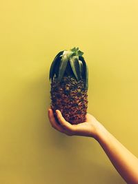 Close-up of hand holding apple against yellow background