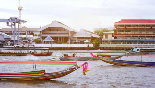 Boats moored on river by buildings against sky