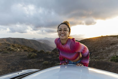 Smiling woman leaning on car roof