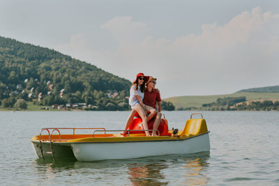 Cheerful man and woman in paddleboat on lake against sky