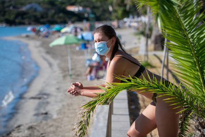 Side view of woman wearing mask standing by railing at beach