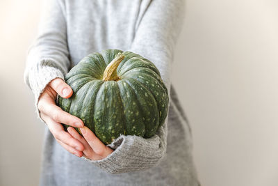 Midsection of woman holding pumpkin against wall