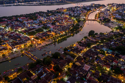 High angle view of illuminated buildings by river against sky