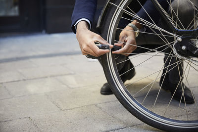 Low section of male commuter locking electric bicycle wheel against building in city