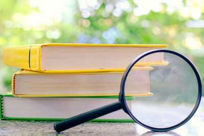 Close-up of magnifying glass by stack of books on table