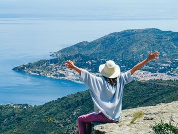 Rear view of woman sitting on cliff against landscape