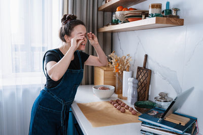 Funny woman making meatballs and talking to her friends via video chat. new normal, social distance