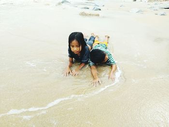 High angle view of siblings lying on shore at beach