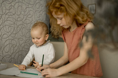Girl teaching sister to draw in book at home