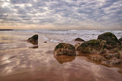 Rocks on beach against sky during sunset