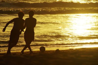 Silhouette boys playing with ball at beach during sunset