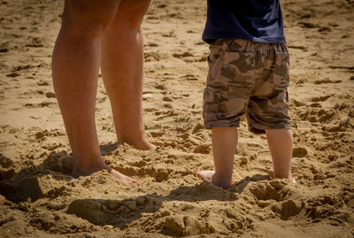 Low section of woman and boy standing on sand at beach