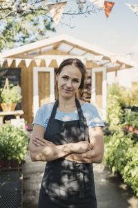 Portrait of confident female owner standing in garden against food store