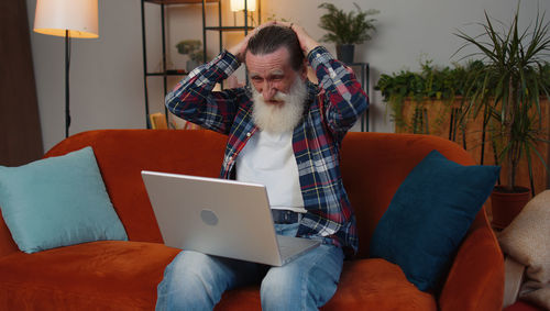 Side view of woman using laptop while sitting on sofa at home