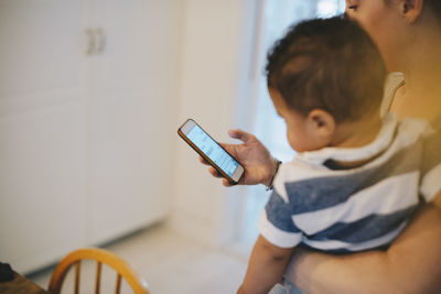 Mother using mobile phone while carrying son at home