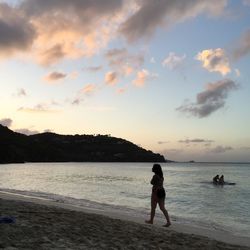 Boys standing on beach against sky during sunset