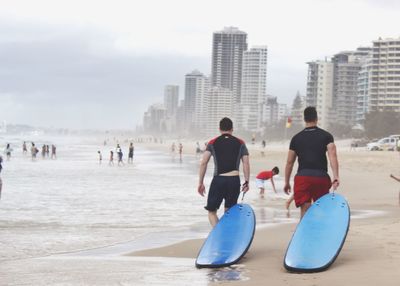 Rear view of men holding blue surfboards while walking on shore