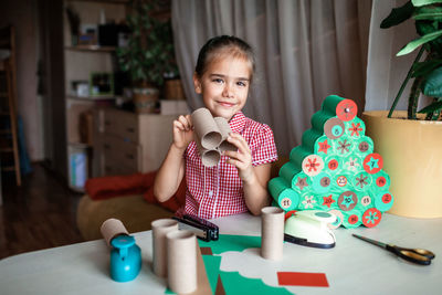 Portrait of girl holding toy while sitting on table at home