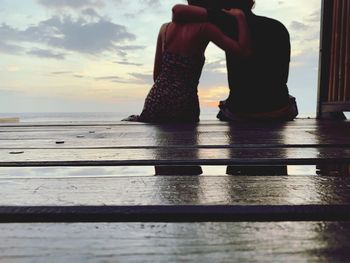 Low section of woman standing on beach against sky during sunset