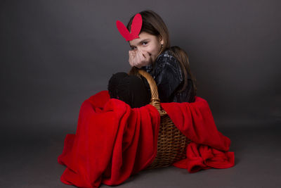 Portrait of smiling girl with costume rabbit ears sitting in basket against gray background