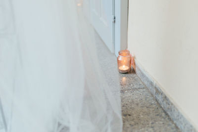 Tea light in glass jar on floor against wall