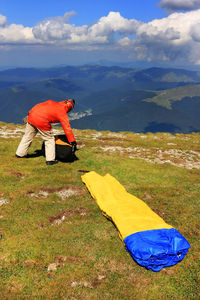 Tent by man holding bag on green mountain during sunny day