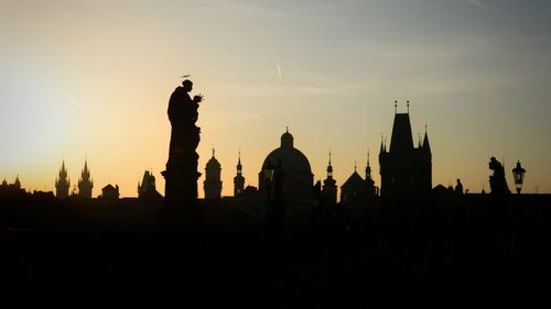 Silhouette temple against buildings during sunset