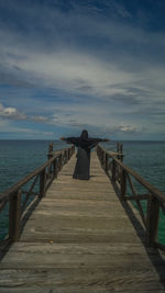 Rear view of person on pier at sea against sky