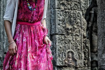 Midsection of woman in pink dress standing against temple at angkor thom