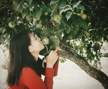Side view of woman kissing apple on tree