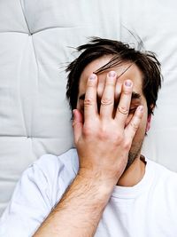Man covering face while lying on bed at home