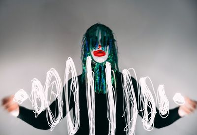 Digital composite image of woman with face paint holding light painting against gray background