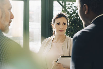 Serious businesswoman listening to male colleagues while standing in office