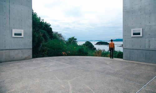 Rear view of man standing by road against sky