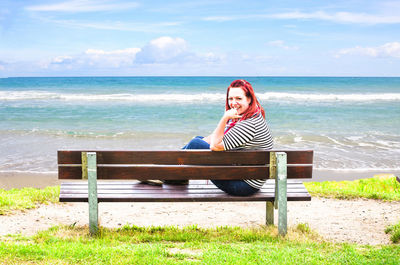 Woman on bench by sea against sky