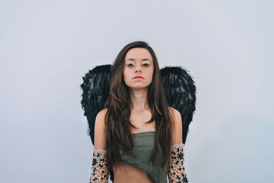 Portrait of beautiful young woman wearing wings against white background
