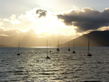 Boats in sea against cloudy sky