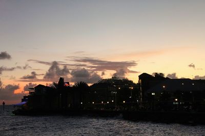 Silhouette buildings by sea against sky during sunset