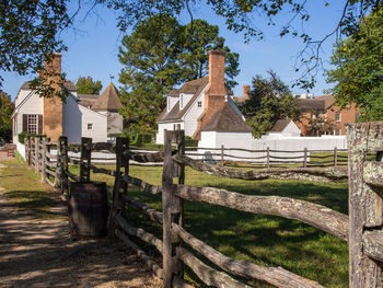 A wooden fence leading to white colonial houses beneath a clear blue sky in williamsburg, virginia.