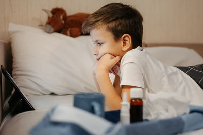 Little boy using tablet while laying in bed in living room. medicines in foreground out of focus