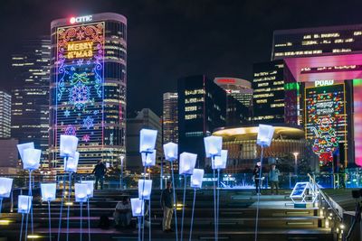 Illuminated modern buildings in city against sky at night
