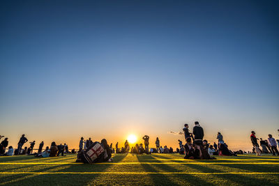 People on land against clear sky during sunset