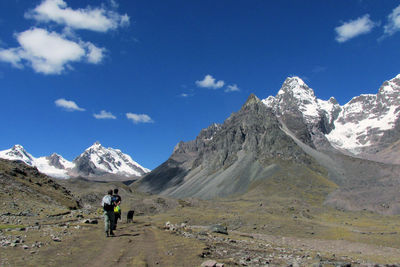 Rear view of men walking towards mountains against sky