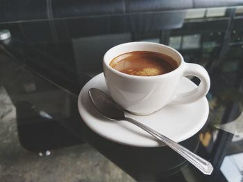 Hot coffee the espresso in white cup on plate and spoon on glasses table in coffee shop.