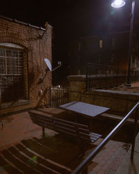 Empty bench by illuminated building at night