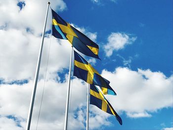 Low angle view of flags waving against cloudy sky