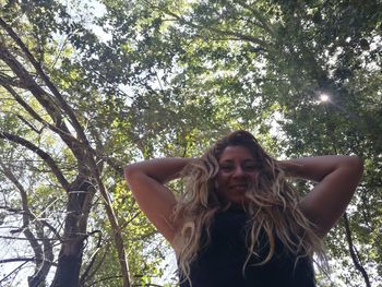 Low angle portrait of young woman standing against trees in forest